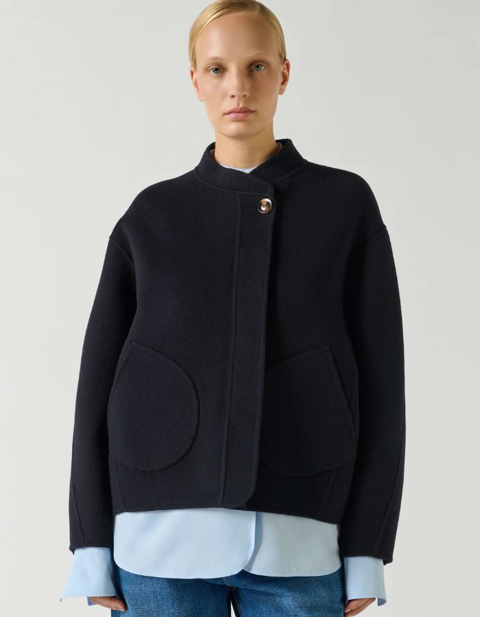 Devant du Manteau court pour femme en laine double face bleu marine profond Deep Navy, modèle Windsor de la marque SOEUR. Présente une coupe ample au volume rond, un col asymétrique, une patte de boutonnage semi-cachée et deux grandes poches plaquées sur le devant.