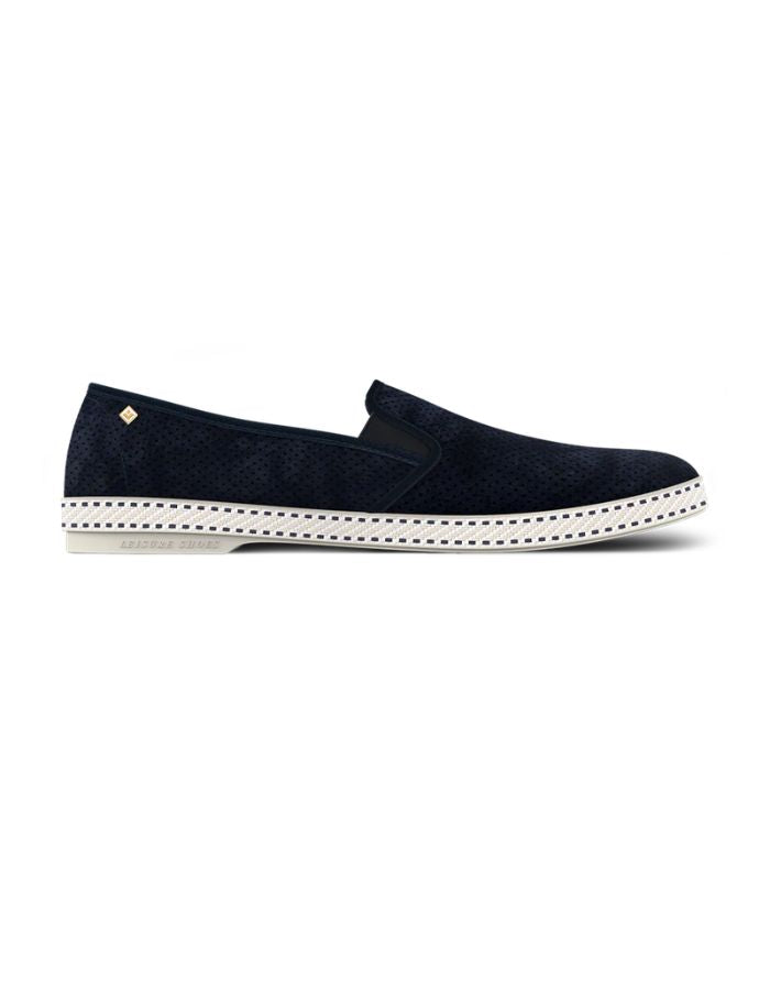 Mocassins Rivieras Classic en daim bleu marine perforé. Semelle blanche contrastée avec couture selle en coton, élastiques de confort et rivet métallique logoté sur le côté. Design intemporel fabriqué en Espagne.