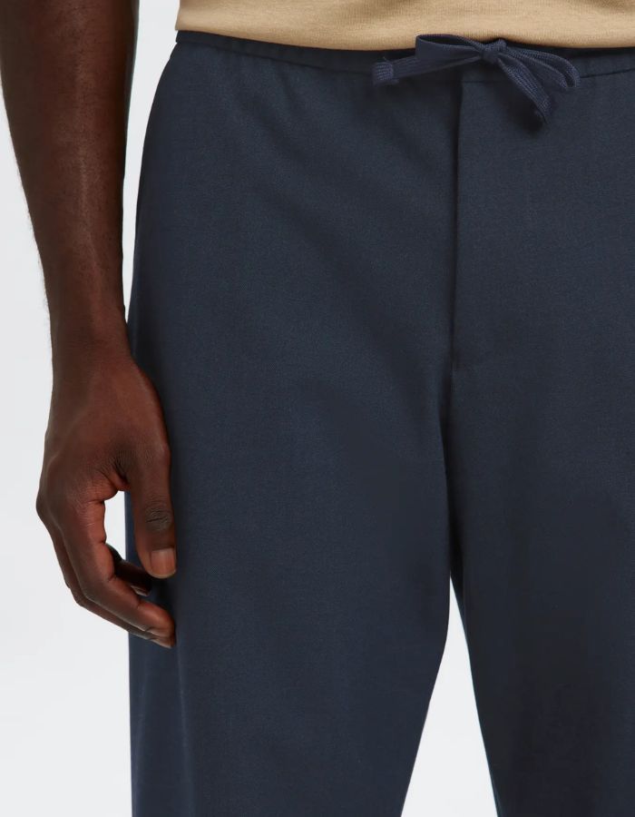 Détail du Pantalon droit pour homme de couleur bleu marine foncé Dark Sapphire, modèle Straight Robert String Pant de la marque Selected. Présente une coupe droite contemporaine, des poches latérales, et une ceinture hybride élastiquée ajustable à l'aide d'un cordon de serrage noir et d'une fermeture par bouton.