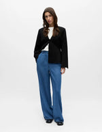 Femme portant un pantalon large fluide denim Frame bleu, taille mi-haute, avec un blazer noir et un t-shirt blanc.