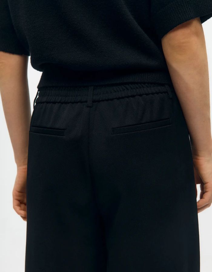 Bassin du Pantalon large pour femme de couleur noir uni opaque, modèle Lisa Wide Pant de la marque Object. Présente une coupe droite très ample de style wide-leg, une taille mi-haute froncée par un élastique confortable et des poches discrètes insérées dans les coutures latérales.