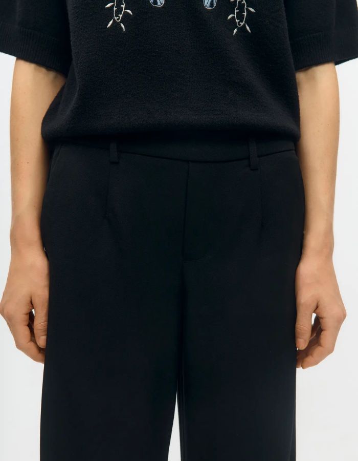 Ceinture du Pantalon large pour femme de couleur noir uni opaque, modèle Lisa Wide Pant de la marque Object. Présente une coupe droite très ample de style wide-leg, une taille mi-haute froncée par un élastique confortable et des poches discrètes insérées dans les coutures latérales.