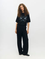 Silhouette avec le Pantalon large pour femme de couleur noir uni opaque, modèle Lisa Wide Pant de la marque Object. Présente une coupe droite très ample de style wide-leg, une taille mi-haute froncée par un élastique confortable et des poches discrètes insérées dans les coutures latérales.