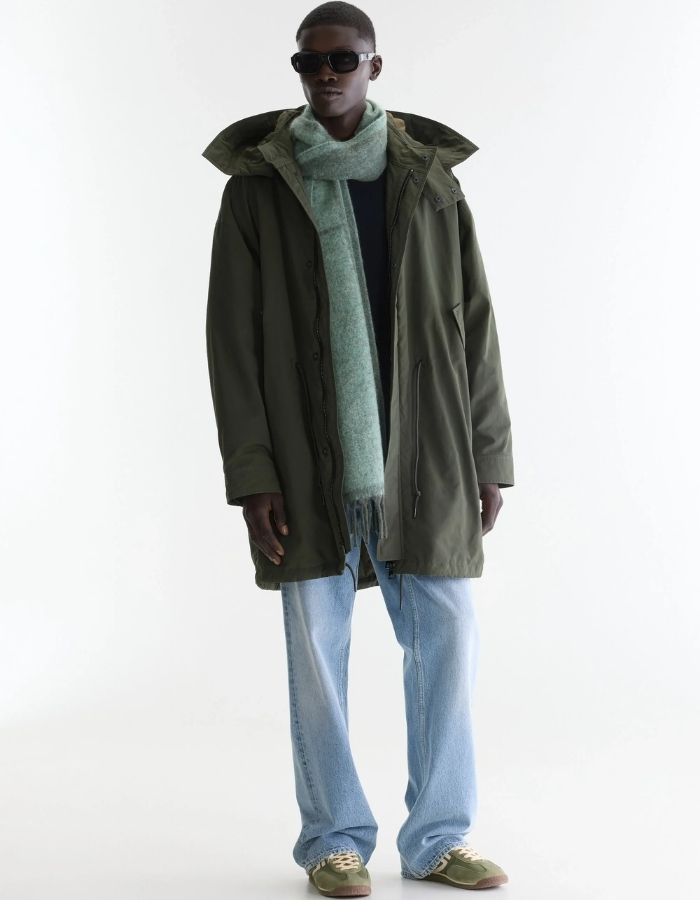 Vue de face de la Parka longue oversize pour homme couleur vert olive foncé avec capuche, fermeture zippée sous pression et poches en biais, modèle Jinx de la marque Bellerose.