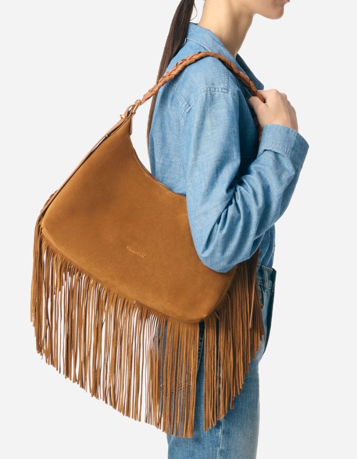 Sac hobo Jess noisette en cuir souple avec longues franges et bandoulière tressée, porté à l'épaule.