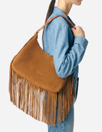 Sac hobo Jess noisette en cuir souple avec longues franges et bandoulière tressée, porté à l'épaule.