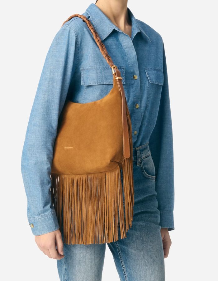 Petit sac hobo Jess noisette en cuir souple avec franges et bandoulière tressée, porté à l'épaule.