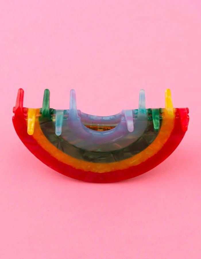 Gros plan sur la Pince à cheveux crabe de taille moyenne de la marque Coucou Suzette en acétate de cellulose brillant. L'accessoire prend la forme d'un arc-en-ciel incurvé aux bandes colorées et nacrées dans les tons rouge, jaune, vert, bleu et violet.