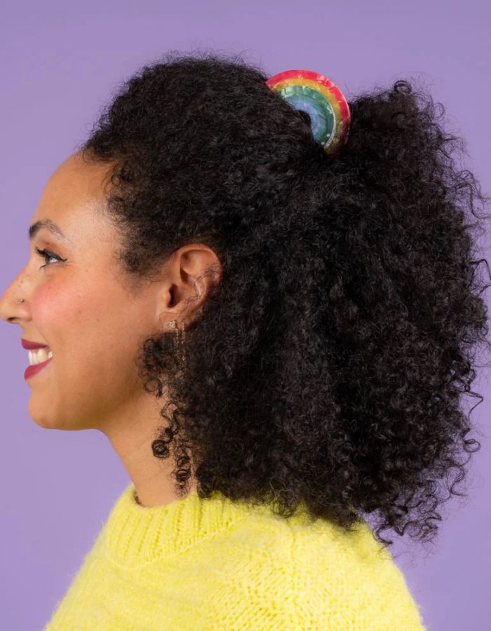 Mise en situation de la Pince à cheveux crabe de taille moyenne de la marque Coucou Suzette en acétate de cellulose brillant. L'accessoire prend la forme d'un arc-en-ciel incurvé aux bandes colorées et nacrées dans les tons rouge, jaune, vert, bleu et violet.