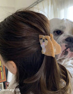 Mise en situation de la Petite pince à cheveux crabe de la marque Coucou Suzette en acétate de cellulose brillant. L'accessoire représente un chien bouledogue anglais marron et blanc de profil avec de jolis bourrelets, des petits yeux noirs et une petite langue rose pendante.