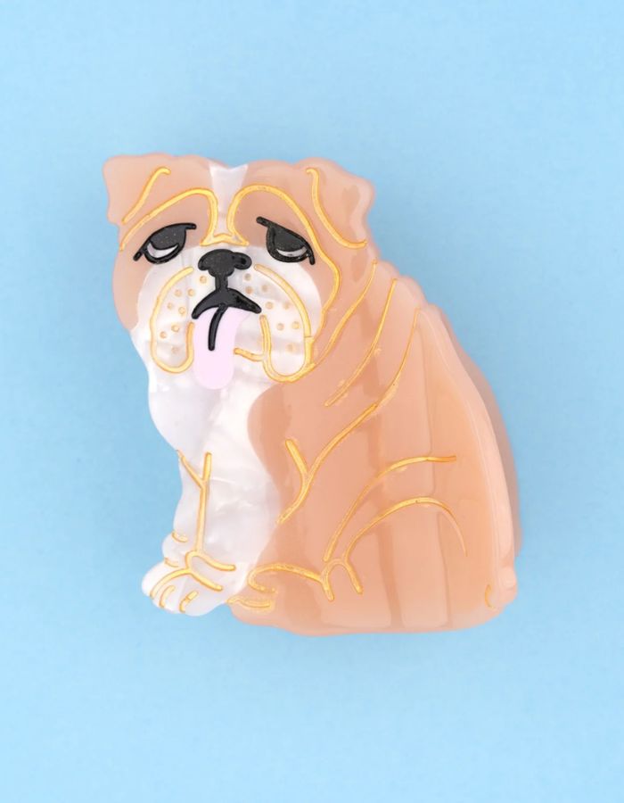 Petite pince à cheveux crabe de la marque Coucou Suzette en acétate de cellulose brillant. L'accessoire représente un chien bouledogue anglais marron et blanc de profil avec de jolis bourrelets, des petits yeux noirs et une petite langue rose pendante.