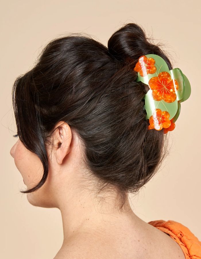Mise en situation de la Grande pince à cheveux XL de la marque Coucou Suzette en acétate de cellulose brillant. L'accessoire est décoré de trois fleurs de capucines orange vif aux détails jaunes et feuilles vertes, idéale pour les cheveux épais.