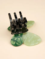Gros plan sur la Pince à cheveux crabe de taille moyenne de la marque Coucou Suzette en acétate de cellulose brillant. L'accessoire prend la forme d'un papillon vert émeraude et vert menthe nacré aux ailes déployées avec des contours graphiques noirs