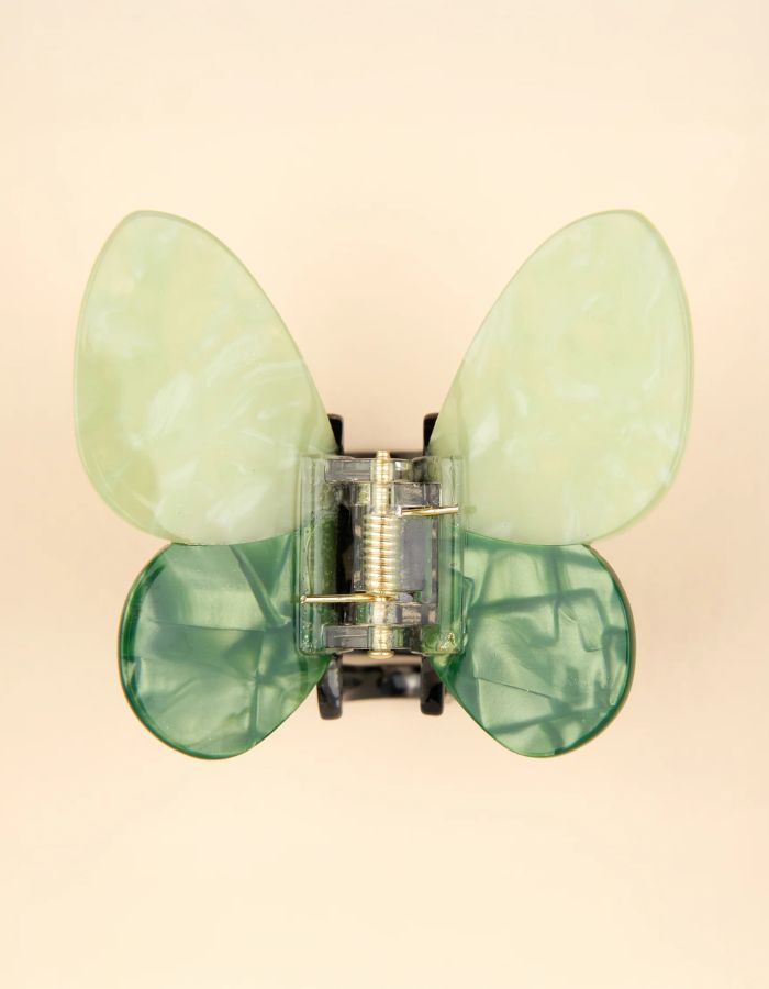 Pince à cheveux crabe de taille moyenne de la marque Coucou Suzette en acétate de cellulose brillant. L'accessoire prend la forme d'un papillon vert émeraude et vert menthe nacré aux ailes déployées avec des contours graphiques noirs