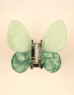 Pince à cheveux crabe de taille moyenne de la marque Coucou Suzette en acétate de cellulose brillant. L'accessoire prend la forme d'un papillon vert émeraude et vert menthe nacré aux ailes déployées avec des contours graphiques noirs