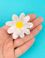 Pince à cheveux Pâquerette blanche et jaune en acétate de cellulose, tenue dans une main.