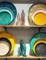 Photo d'ambiance dugrand plateau décoratif rond Molitor par Bazardeluxe, grand format de 60 cm de diamètre. Finition émaillée brillante de couleur vert amande doux, orné d'un fond aux motifs géométriques en relief.