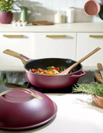 La Fabuleuse Poêle Cookut 28cm aubergine avec poignée en bois, remplie de légumes colorés, sur une plaque de cuisson.