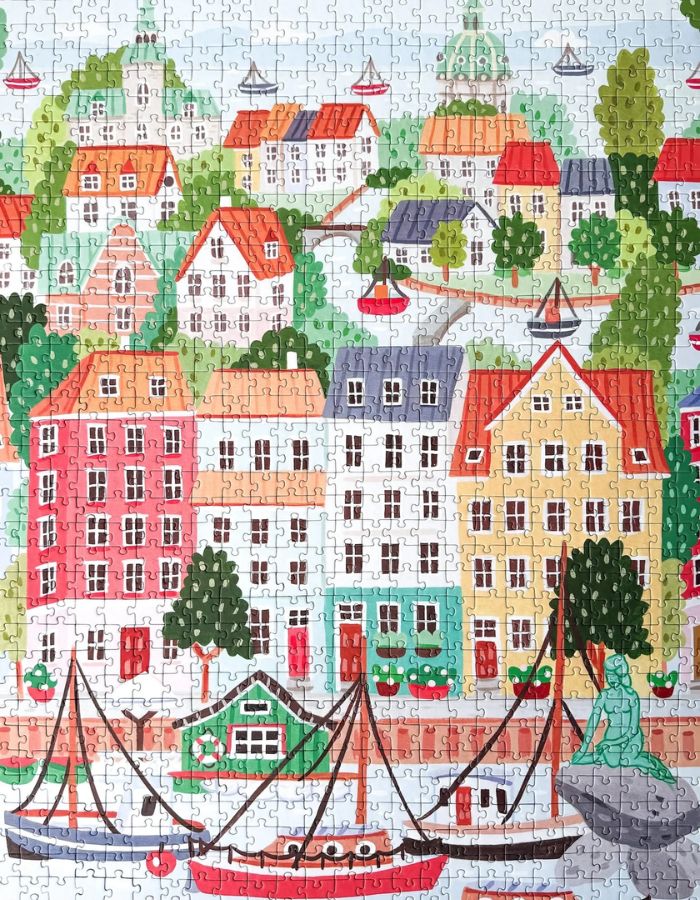 Puzzle de 1000 pièces pour adulte illustré par Serena White pour Piecely, représentant les canaux et les façades colorées de Copenhague au crépuscule. Présenté à côté de sa boîte de rangement élégante et écoresponsable.