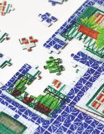 Détail du Puzzle de 1000 pièces pour adulte illustré par Mélanie Voituriez pour Piecely, représentant une rue colorée de Lisbonne avec le tramway jaune traditionnel et des façades en azulejos. Présenté aux côtés de sa boîte de rangement écoresponsable.
