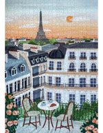 Vue dupuzzle 1000 pièces Paris de la marque Piecely. L'illustration représente une table de petit-déjeuner sur un balcon avec croissants et café, offrant une vue romantique sur les toits de Paris et la Tour Eiffel au lever du soleil.