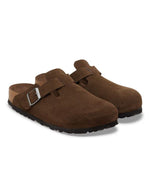 Paire de Sabots fermés modèle Boston de la marque Birkenstock en cuir velours souple de couleur marron foncé Carafe. Présente une bride ajustable à boucle métallique sur le dessus et une semelle anatomique ton sur ton en liège avec lit de pied souple, version chaussant étroit.