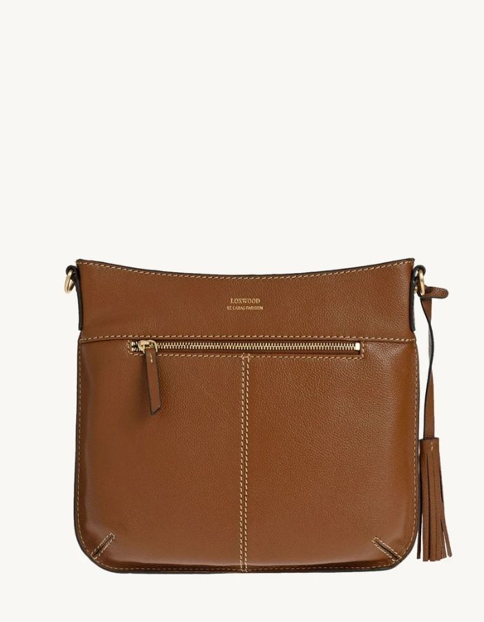 Dos du sac besace pour femme en cuir grainé camel brandy avec logo L micro-perforé, pompon assorti et bandoulière réglable, modèle Celia L de la marque Loxwood
