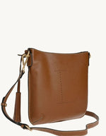Profil du sac besace pour femme en cuir grainé camel brandy avec logo L micro-perforé, pompon assorti et bandoulière réglable, modèle Celia L de la marque Loxwood