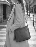 Femme portant le sac besace pour femme en cuir grainé camel brandy avec logo L micro-perforé, pompon assorti et bandoulière réglable, modèle Celia L de la marque Loxwood