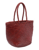 Vue du côté du petit sac panier Grace Basket de Dragon Diffusion en cuir tressé bordeaux, forme arrondie galbée avec tissage en diagonale et poignées tressées.