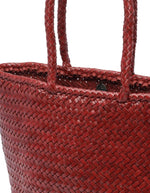 Vue du dessus du petit sac panier Grace Basket de Dragon Diffusion en cuir tressé bordeaux, forme arrondie galbée avec tissage en diagonale et poignées tressées.