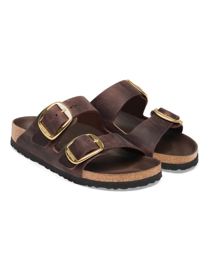Paire de Sandales Birkenstock modèle Arizona Big Buckle avec chaussant étroit. Présente deux larges brides en cuir huilé épais à bords bruts dotées de grandes boucles métalliques élégantes, montées sur la célèbre semelle anatomique en liège et cuir lisse assorti.