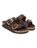 Paire de Sandales Birkenstock modèle Arizona Big Buckle avec chaussant étroit. Présente deux larges brides en cuir huilé épais à bords bruts dotées de grandes boucles métalliques élégantes, montées sur la célèbre semelle anatomique en liège et cuir lisse assorti.