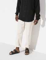 Silhouette homme portant des Sandales anatomiques à deux brides noires pour homme et femme, tige en Birko-Flor avec boucles réglables et semelle en liège, modèle Arizona Narrow Black de Birkenstock.