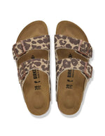Dessus des Sandales d'été pour femme modèle Arizona de la marque Birkenstock, en cuir velours à imprimé léopard Leo Sandcastle beige et marron. Présentent deux brides larges réglables avec des boucles en métal noir et la célèbre semelle anatomique en liège naturel.