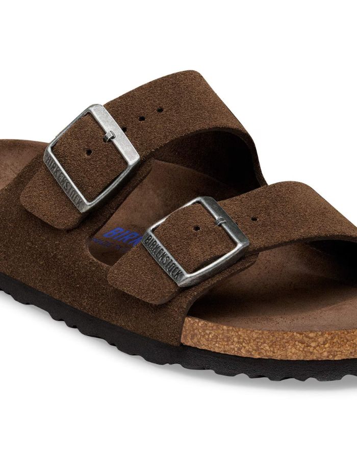 Boucle des Sandales Birkenstock modèle Arizona avec chaussant étroit. Présente deux brides ajustables en cuir velours souple de couleur marron foncé Carafe avec des boucles en métal assorties, montées sur la célèbre semelle anatomique en liège avec lit de pied souple.