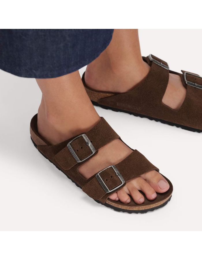 Dessus des Sandales Birkenstock modèle Arizona avec chaussant étroit. Présente deux brides ajustables en cuir velours souple de couleur marron foncé Carafe avec des boucles en métal assorties, montées sur la célèbre semelle anatomique en liège avec lit de pied souple.