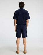 Homme de dos portant un short marine en éponge avec un t-shirt assorti et des sandales.