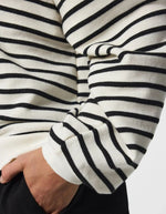 Manche du Sweatshirt à col rond et manches longues pour femme de couleur écru blanc cassé Cloud Dancer, modèle Greta de la marque PIECES. Présente une coupe classique droite avec un petit cœur noir brodé sur le côté gauche de la poitrine.
