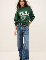 Mannequin portant un sweatshirt Fenja Emeraude vert foncé Ba&sh avec logo blanc, coupe courte et ample, et un jean large.