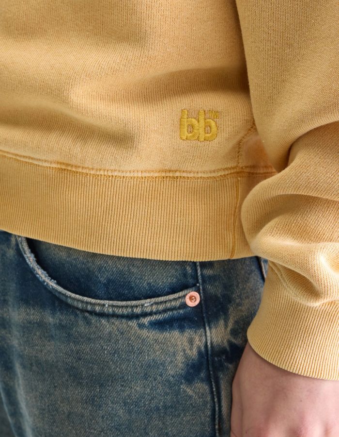 Sweatshirt Fella Sunlight jaune moutarde en molleton de coton avec broderie "bb" et bords-côtes, porté avec un jean.