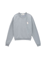 Sweat-shirt pour femme en molleton doux de couleur bleu glacier pastel, modèle Swing de la marque Ba&sh. Présente une coupe ample loose avec col rond et manches raglan, rehaussée de surpiqûres overlock et d'une impression signature Ba&sh texturée sur la poitrine.