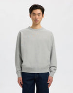 Vue de face du Sweatshirt col rond pour homme en coton biologique gris clair chiné Light Grey Melange, modèle Relaxluke de la marque SELECTED HOMME. Présente une coupe droite avec finition en bord-côte au col, aux poignets et à la taille