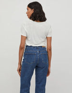 Femme portant un t-shirt blanc col V en jersey et un jean bleu foncé.