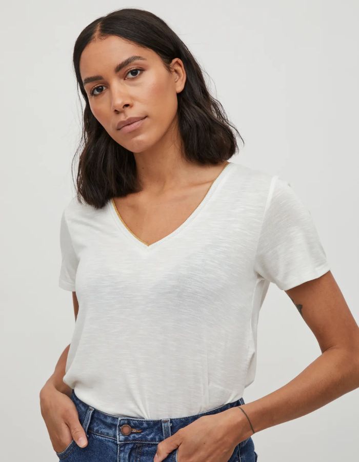 Femme portant un t-shirt blanc col V en jersey, avec un liseré doré subtil à l'encolure.