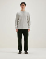 Homme portant un t-shirt gris clair en jersey double face à manches longues et un pantalon vert foncé.