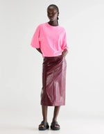 Mannequin portant un t-shirt VOSS Fluo Pink en coton, coupe cropped relaxed, avec une jupe midi bordeaux effet croco.