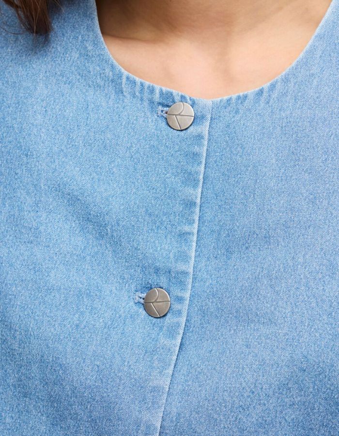 Détail du Top court en jean bleu clair Delila de ROUGE EDIT. Modèle à manches courtes bouffantes, encolure ronde et fermeture par boutons sur le devant. Coupe regular en coton denim.