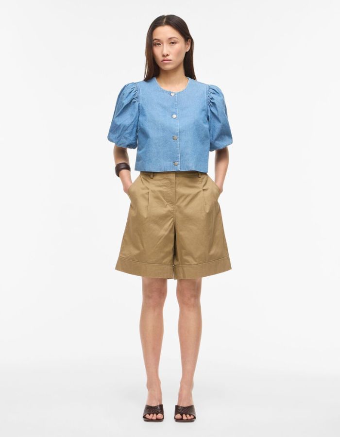 Silhouette avec le Top court en jean bleu clair Delila de ROUGE EDIT. Modèle à manches courtes bouffantes, encolure ronde et fermeture par boutons sur le devant. Coupe regular en coton denim.