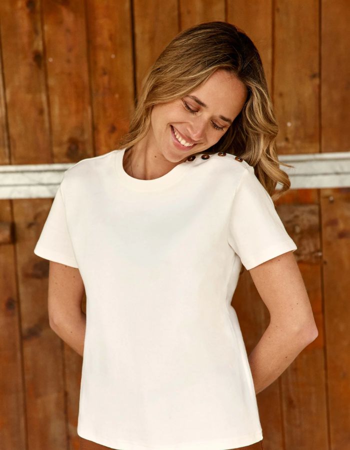 Vue de face du T-shirt écru col rond pour femme en coton, modèle Taiga de la marque LA PETITE ÉTOILE. Présente une coupe droite à manches courtes et un boutonnage aspect corne sur l'épaule gauche.